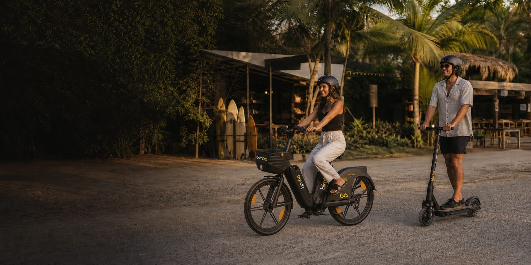 Helmeted Bimba e-bike and e-scooter riders passing a surf cafe in Santa Teresa