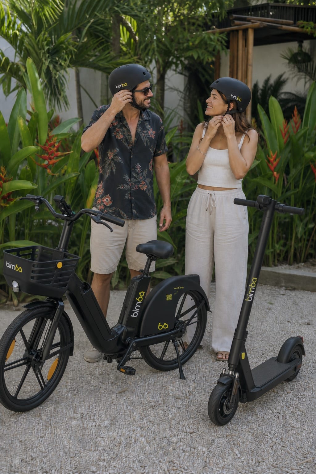 Un hombre y una mujer se ponen cascos Bimba junto a una bicicleta eléctrica y un scooter OKAI ES400A en Santa Teresa