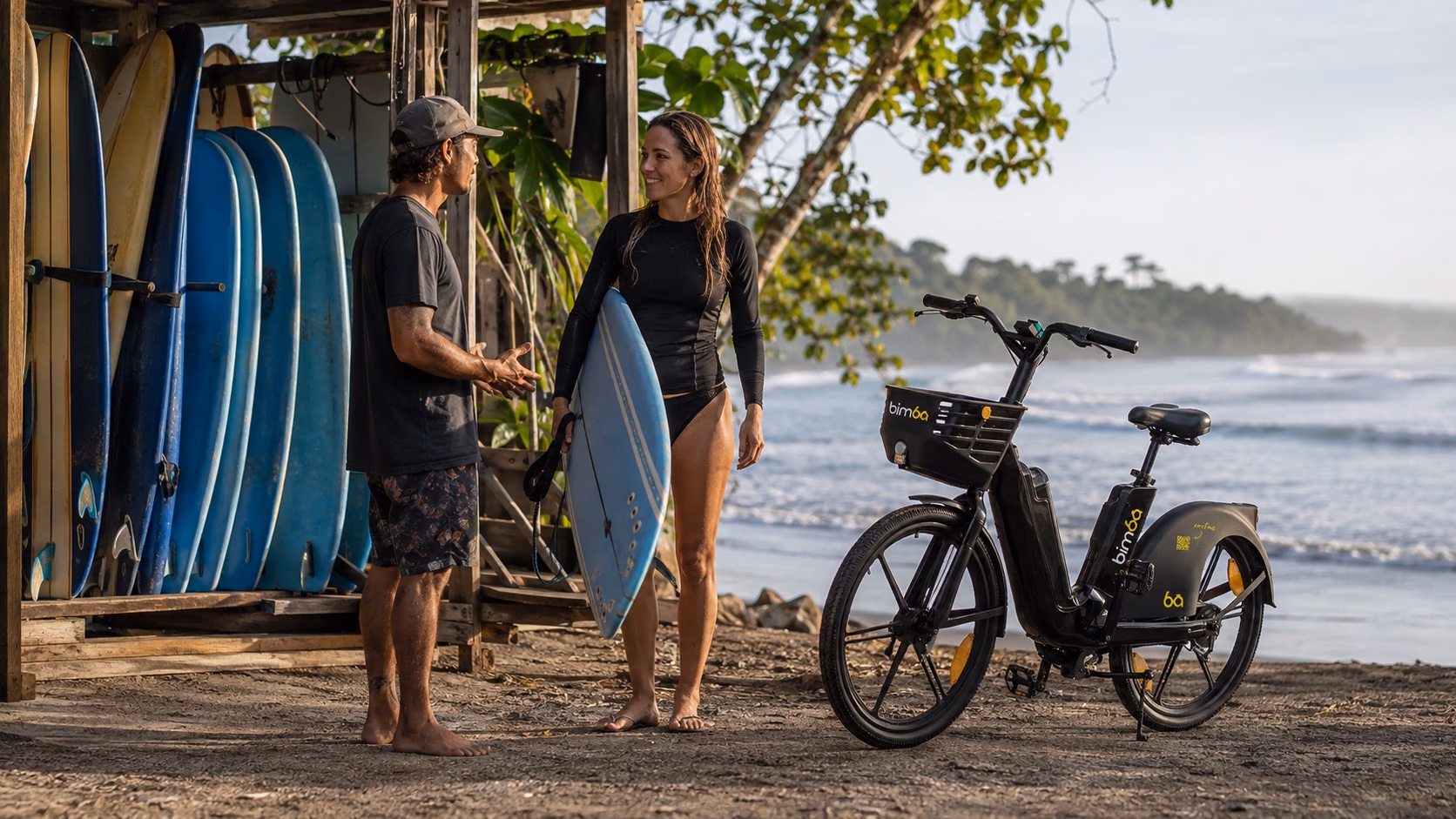 Beginner surfer meeting an instructor beside an exact-model Bimba e-bike at Playa Carmen