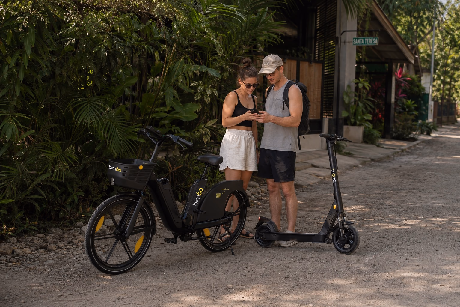 Travelers checking an accommodation location beside exact-model Bimba electric bike and scooter in Santa Teresa