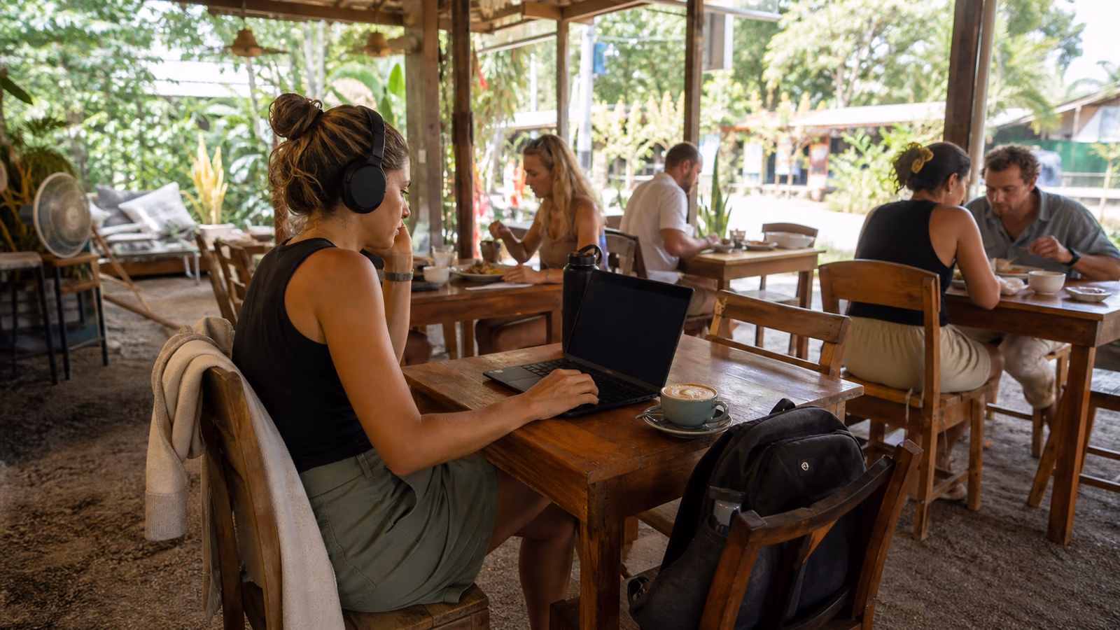 Traveler working quietly with headphones, a laptop and an ordered coffee at an open-air tropical café