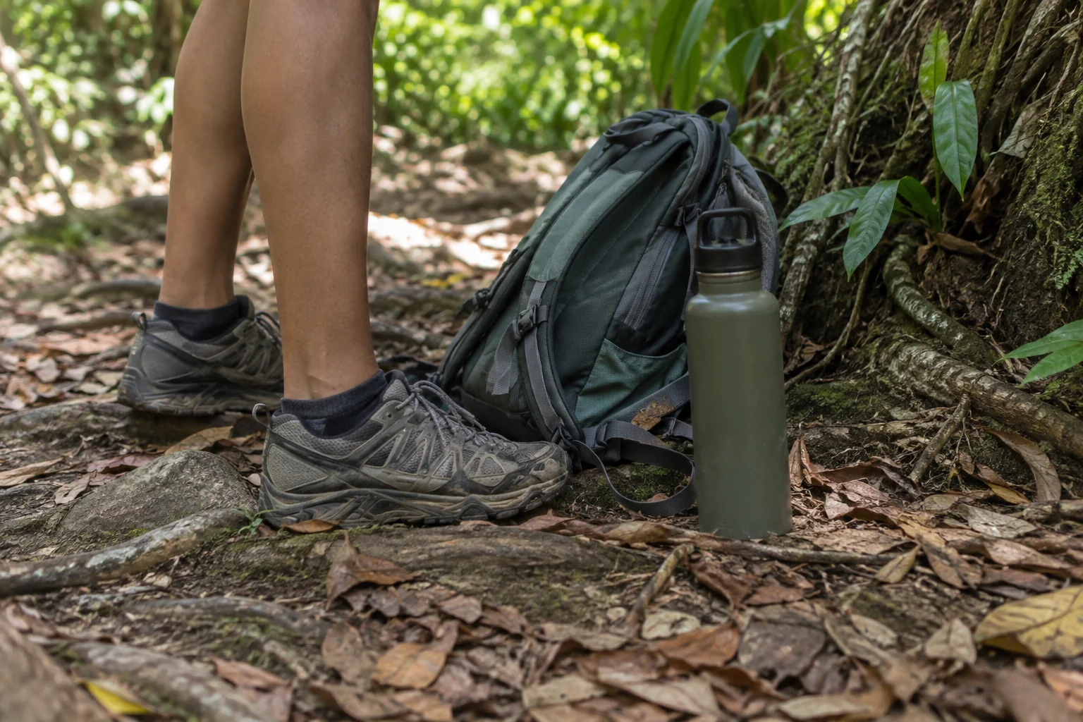 Walking shoes, water and a daypack beside a forest trail